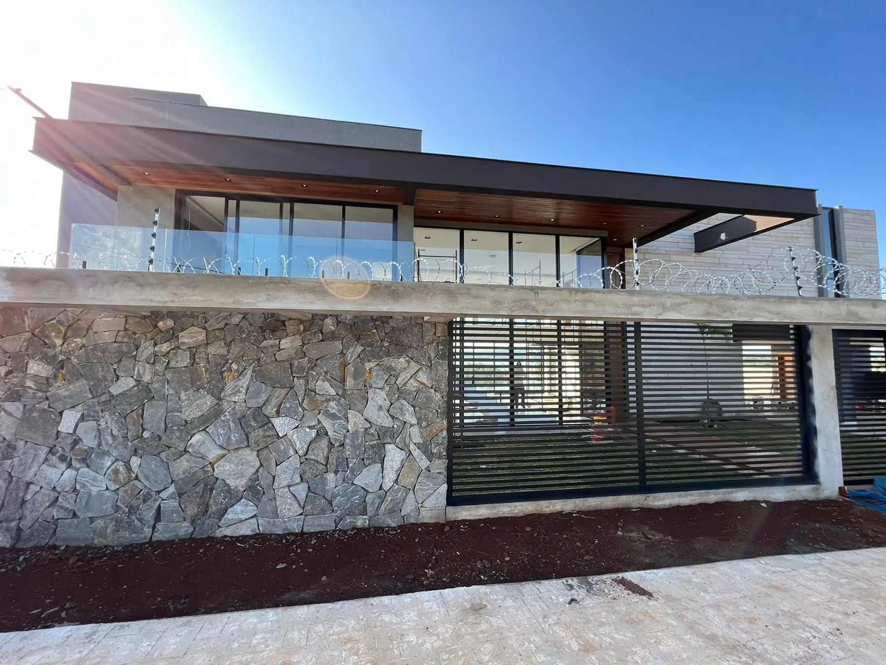 Casa M&G: residência de alto padrão com fachada em pedra, beiral em madeira e esquadrias de piso a teto